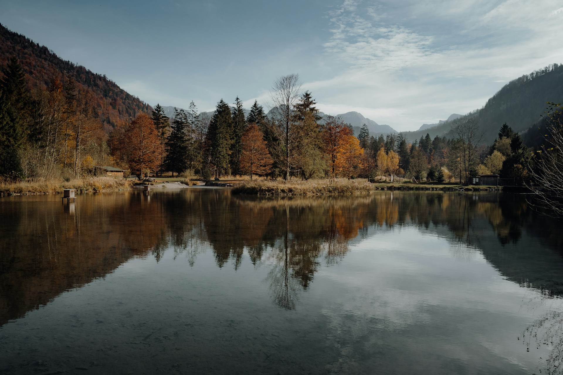 Ruhiger See im Herbst mit Bäumen und Bergen im Hintergrund